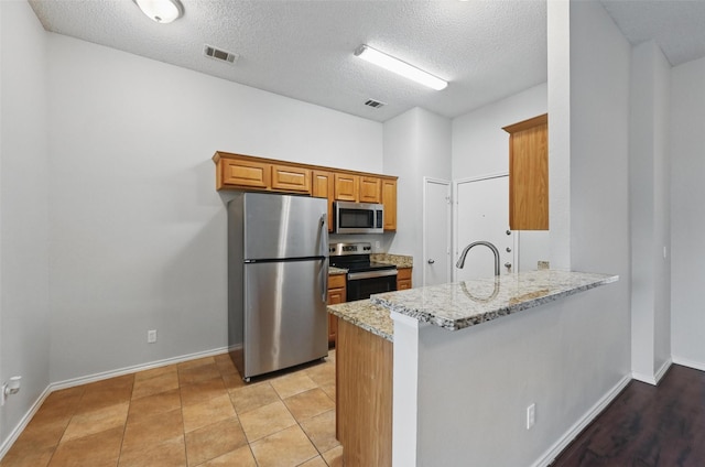 1412 Mockingbird Ln, Desoto, TX 75115 - kitchen featuring stainless steel appliances, brown cabinetry, a peninsula, a textured ceiling, and light stone counters