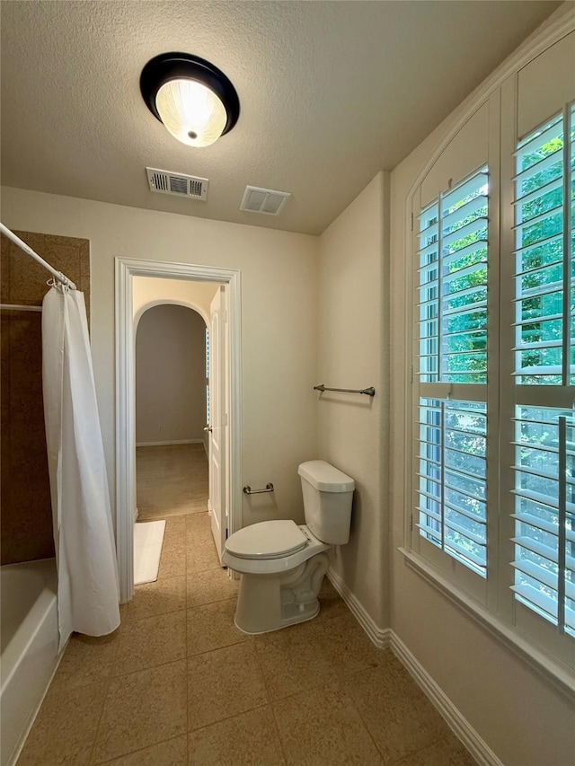 4561 Firewheel Dr, Plano, TX 75024 - bathroom featuring toilet, a textured ceiling, baseboards, and shower / bath combination with curtain