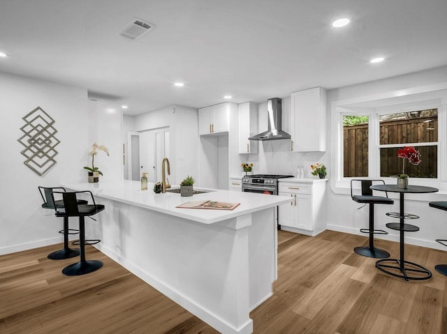2371 Chart Dr, Dallas, TX 75228 - kitchen with wall chimney range hood, light wood-style floors, a peninsula, white cabinets, and stainless steel range with gas stovetop