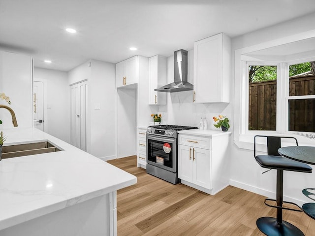 2371 Chart Dr, Dallas, TX 75228 - kitchen featuring wall chimney range hood, stainless steel gas stove, a sink, light wood finished floors, and white cabinets
