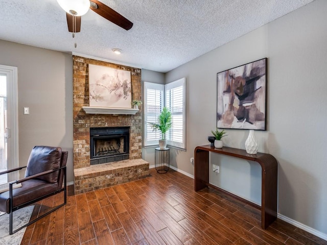 46 Morrow Dr, Bedford, TX 76021 - living room featuring a textured ceiling, a brick fireplace, baseboards, wood finished floors, and ceiling fan