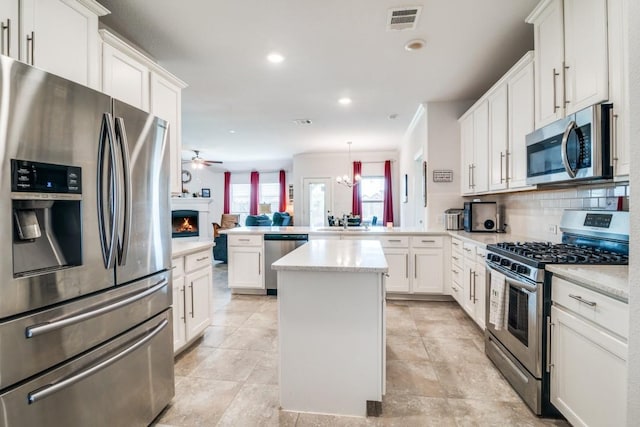 324 Jefferson Ln, Fate, TX 75189 - kitchen with stainless steel appliances, a peninsula, a ceiling fan, decorative backsplash, and a kitchen island