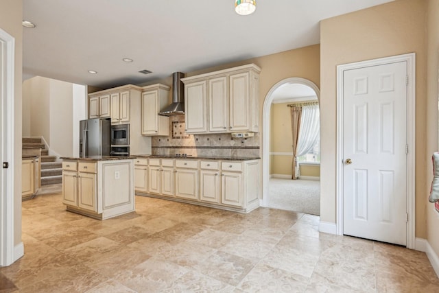 604 Nelson Ct, Plano, TX 75025 - kitchen featuring cream cabinetry, stainless steel appliances, wall chimney range hood, arched walkways, and backsplash