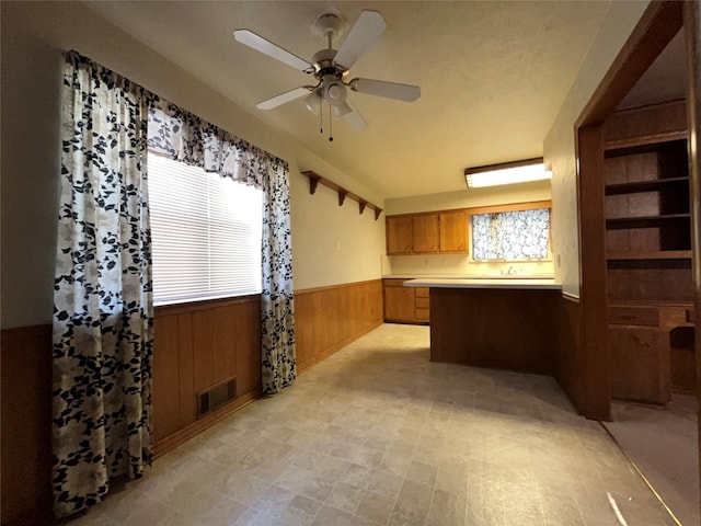 3614 Matador Dr, Garland, TX 75042 - kitchen featuring wainscoting, a peninsula, brown cabinets, ceiling fan, and wooden walls