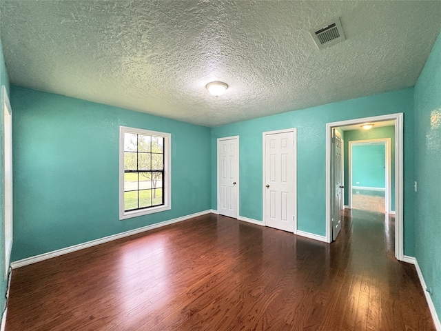 1205 Lamar, Mount Pleasant, TX 75455 - unfurnished bedroom with dark wood-style floors, a textured ceiling, two closets, and baseboards