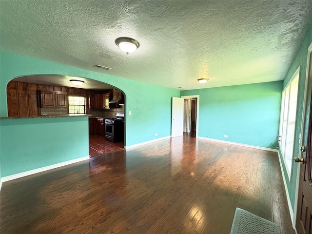 1205 Lamar, Mount Pleasant, TX 75455 - unfurnished living room featuring arched walkways, dark wood finished floors, baseboards, and a textured ceiling
