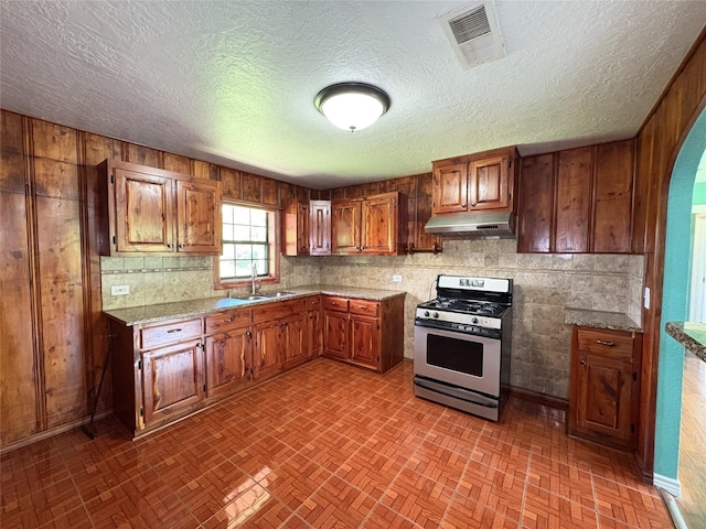 1205 Lamar, Mount Pleasant, TX 75455 - kitchen featuring stainless steel gas range oven, under cabinet range hood, brick patterned flooring, a sink, and brown cabinetry