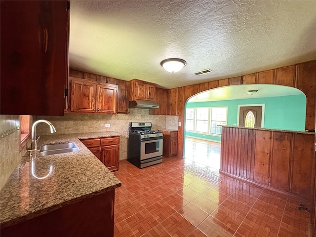 1205 Lamar, Mount Pleasant, TX 75455 - kitchen featuring gas stove, under cabinet range hood, a sink, arched walkways, and brown cabinets