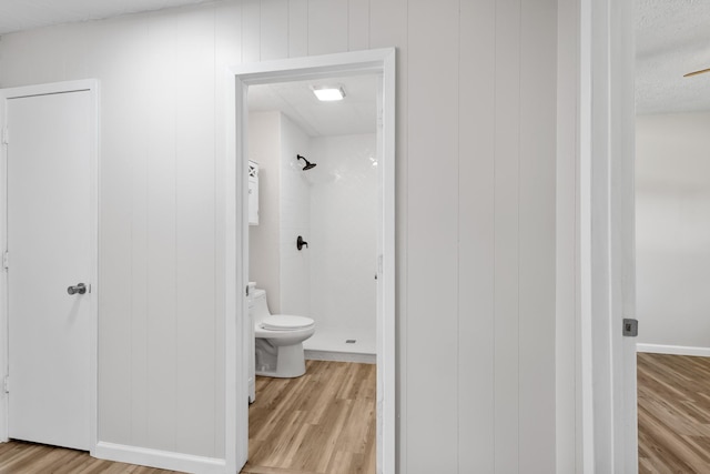 903 1st St, Bridgeport, TX 76426 - bathroom featuring a tile shower, wood finished floors, toilet, a textured ceiling, and baseboards