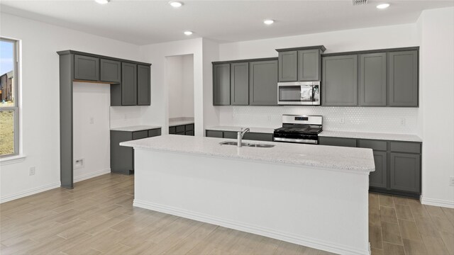 7545 Wild Mint Trl, Midlothian, TX 76084 - kitchen with stainless steel appliances, a sink, backsplash, light wood-type flooring, and a kitchen island with sink