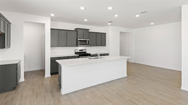 7545 Wild Mint Trl, Midlothian, TX 76084 - kitchen with appliances with stainless steel finishes, a sink, decorative backsplash, light wood-style floors, and a kitchen island with sink