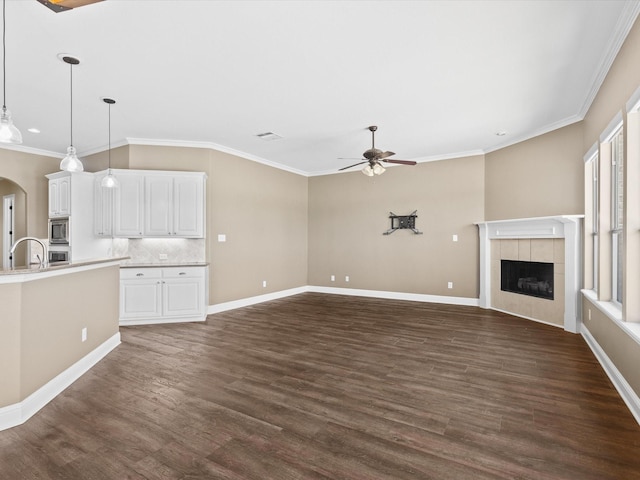 1105 Crown Valley Dr, Weatherford, TX 76087 - unfurnished living room with ceiling fan, a tiled fireplace, dark wood-type flooring, baseboards, and ornamental molding