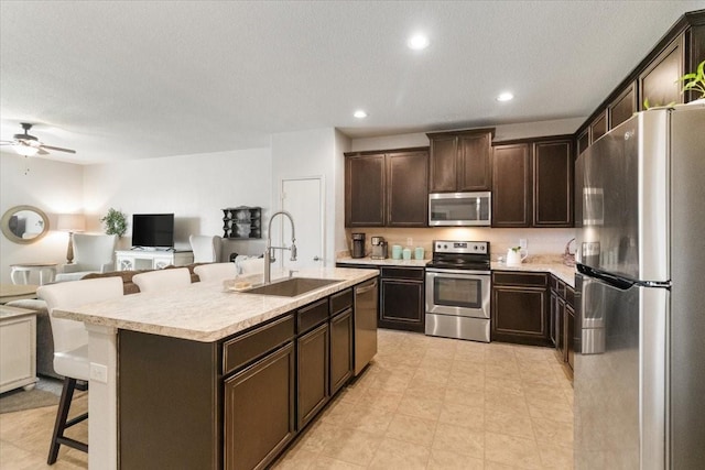 2113 Brenham Dr, Forney, TX 75126 - kitchen featuring stainless steel appliances, a sink, open floor plan, a kitchen bar, and dark brown cabinets
