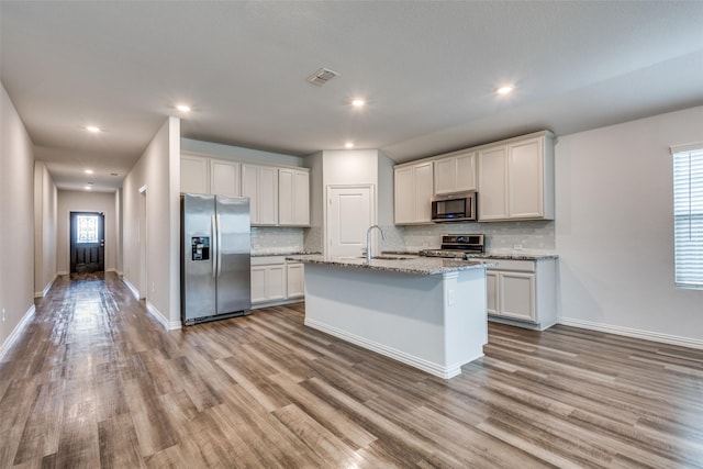788 Cascade Ln, Princeton, TX 75407 - kitchen featuring appliances with stainless steel finishes, a sink, decorative backsplash, wood finished floors, and a center island with sink