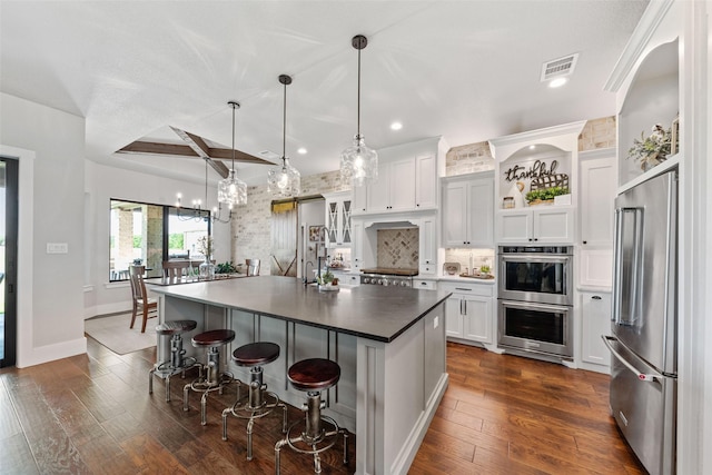 139 County Road 2525, Decatur, TX 76234 - kitchen with stainless steel appliances, white cabinets, a kitchen island with sink, a kitchen bar, and backsplash