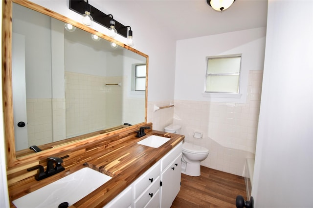 2013 S High St, Brady, TX 76825 - bathroom with toilet, tile walls, double vanity, wood finished floors, and wainscoting