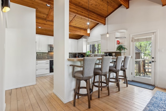 215 N Beverly Dr, Malakoff, TX 75148 - kitchen featuring stainless steel microwave, white cabinets, light wood finished floors, a wooden ceiling with exposed beams, and a breakfast bar