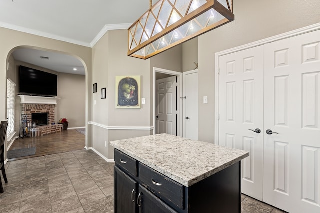 305 Margaret St, Fate, TX 75189 - kitchen featuring dark cabinets, arched walkways, crown molding, a center island, and a fireplace
