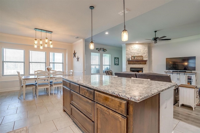 128 Colonial Dr, Joshua, TX 76058 - kitchen with ornamental molding, a stone fireplace, a ceiling fan, pendant lighting, and a center island