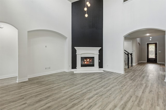 716 Field Xing, Little Elm, TX 76227 - unfurnished living room with a towering ceiling, light wood finished floors, a glass covered fireplace, stairs, and baseboards