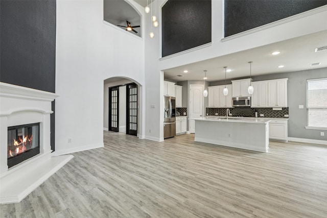 716 Field Xing, Little Elm, TX 76227 - unfurnished living room with light wood-style floors, arched walkways, a sink, a glass covered fireplace, and a ceiling fan