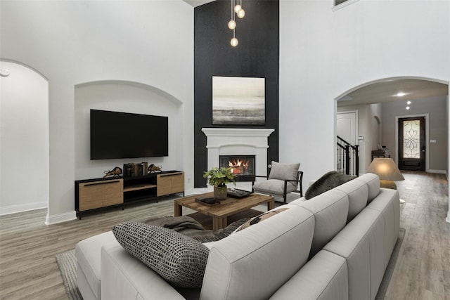 716 Field Xing, Little Elm, TX 76227 - living area featuring arched walkways, a high ceiling, stairway, light wood-style flooring, and a glass covered fireplace
