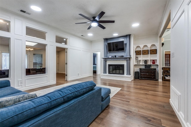 10220 Shadow Way, Dallas, TX 75243 - living room with a fireplace, a ceiling fan, a decorative wall, wood finished floors, and recessed lighting