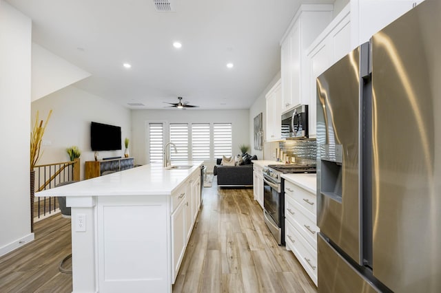 2734 Levee Ln, Lewisville, TX 75067 - kitchen with appliances with stainless steel finishes, open floor plan, a sink, light wood-style flooring, and white cabinets