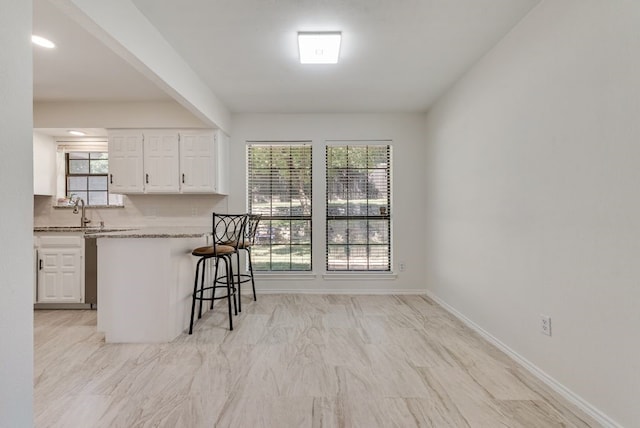 7020 Live Oak Dr, North Richland Hills, TX 76182 - kitchen with white cabinets, a kitchen breakfast bar, a sink, light stone countertops, and backsplash