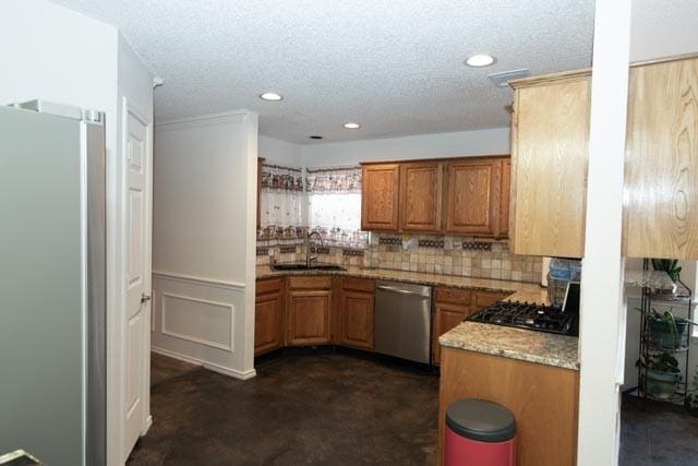 1111 Bayshore St, Allen, TX 75002 - kitchen featuring appliances with stainless steel finishes, a sink, brown cabinetry, decorative backsplash, and a textured ceiling