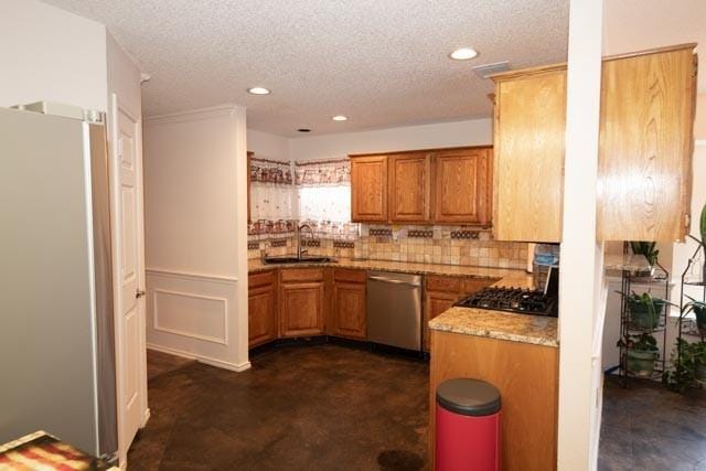 1111 Bayshore St, Allen, TX 75002 - kitchen featuring appliances with stainless steel finishes, a sink, brown cabinetry, a textured ceiling, and recessed lighting