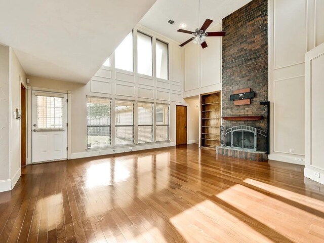 1101 Shawnee Trl, Carrollton, TX 75007 - unfurnished living room with a towering ceiling, wood finished floors, ceiling fan, a large fireplace, and baseboards
