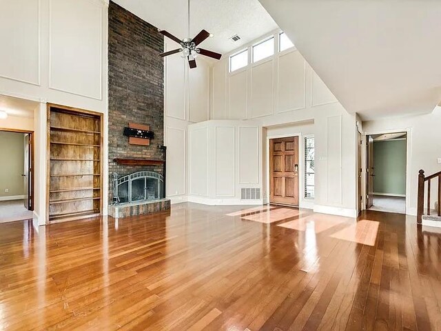 1101 Shawnee Trl, Carrollton, TX 75007 - unfurnished living room with a towering ceiling, a decorative wall, ceiling fan, built in features, and wood-type flooring