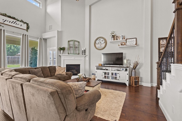 3620 Brahman Ct, Mckinney, TX 75071 - living room with stairs, dark wood-style flooring, a glass covered fireplace, a high ceiling, and baseboards