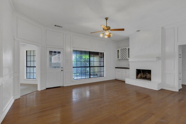 225 Wildwood Dr, Desoto, TX 75115 - unfurnished living room with a decorative wall, a ceiling fan, dark wood-style flooring, a brick fireplace, and ornamental molding
