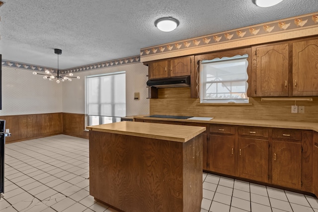 7725 Westwind Dr, Fort Worth, TX 76179 - kitchen with under cabinet range hood, light countertops, a textured ceiling, wainscoting, and a chandelier