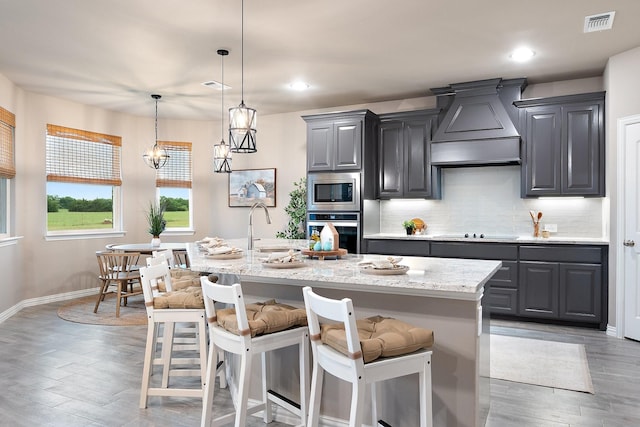 123 Cedar Elm Ln, Nevada, TX 75173 - kitchen featuring stainless steel appliances, custom range hood, a breakfast bar, a kitchen island with sink, and light wood-style floors