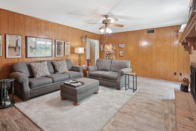 10930 Ridgemeadow Dr, Dallas, TX 75218 - living area featuring a ceiling fan, wood walls, wood finished floors, a textured ceiling, and a brick fireplace