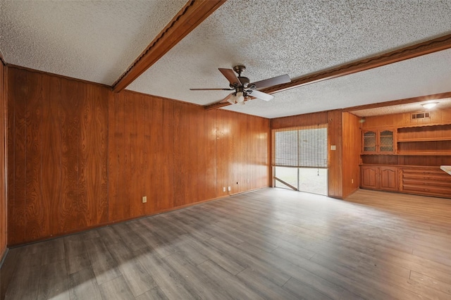 6330 Autumn Woods Trl, Dallas, TX 75232 - unfurnished living room featuring a textured ceiling, wooden walls, ceiling fan, wood finished floors, and beamed ceiling