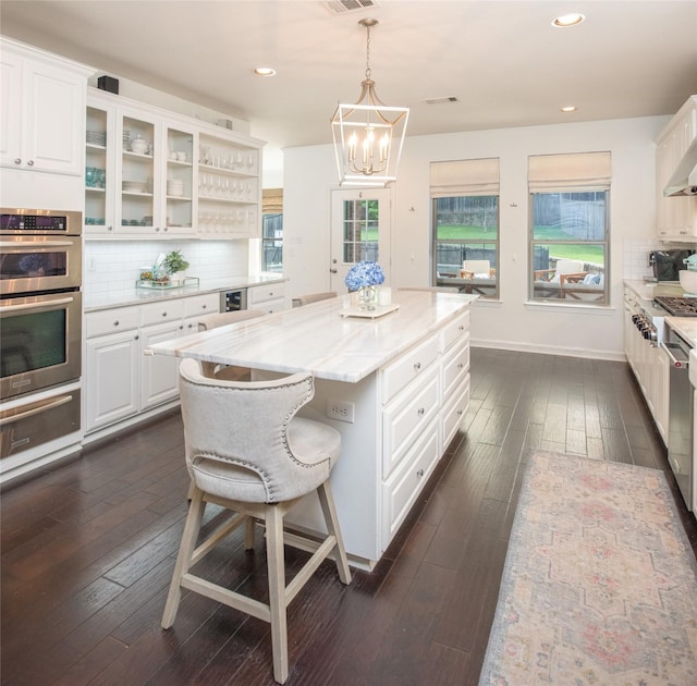 7002 Clear Springs Pkwy, Garland, TX 75044 - kitchen with double oven, a warming drawer, dark wood-type flooring, white cabinetry, and decorative backsplash