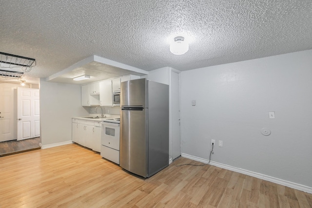 408 E Baylor St, Weatherford, TX 76086 - kitchen featuring appliances with stainless steel finishes, a sink, light wood-type flooring, white cabinets, and a textured ceiling