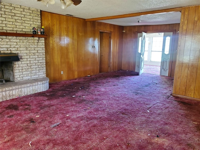 8740 County Road 2403, Tool, TX 75143 - unfurnished living room featuring wooden walls, carpet floors, a brick fireplace, a textured ceiling, and a ceiling fan