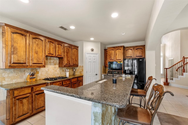 15534 Fox Meadow Ln, Frisco, TX 75035 - kitchen with a sink, black appliances, arched walkways, light tile patterned floors, and brown cabinetry