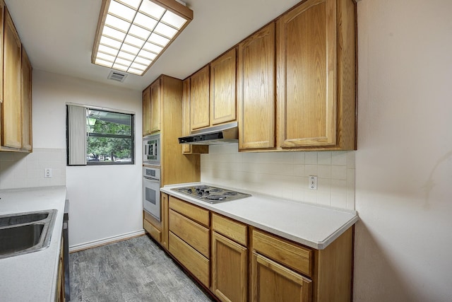 2947 Sinbad Cir, Farmers Branch, TX 75234 - kitchen with under cabinet range hood, appliances with stainless steel finishes, a sink, tasteful backsplash, and light countertops