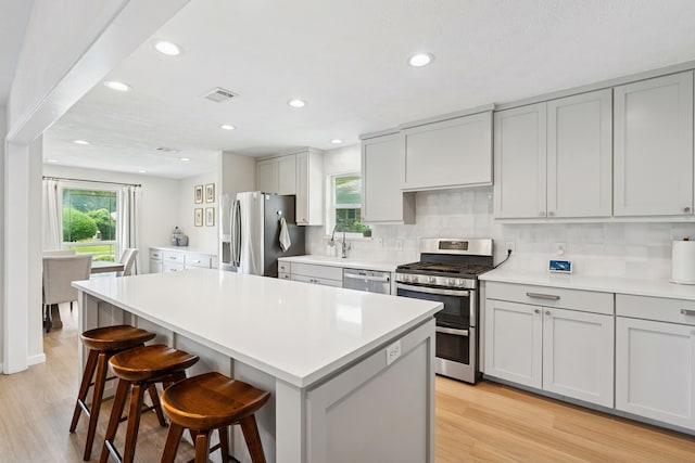 328 High Brook Dr, Richardson, TX 75080 - kitchen with stainless steel appliances, a kitchen bar, decorative backsplash, light wood-type flooring, and a kitchen island