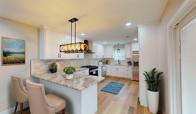 2210 Mcclure St, Irving, TX 75062 - kitchen with black gas range, wall chimney exhaust hood, stainless steel dishwasher, white cabinetry, and backsplash