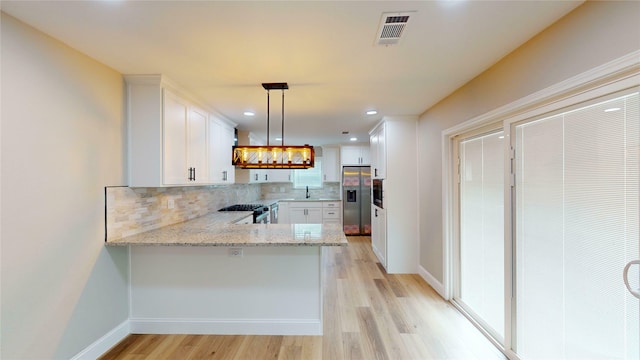 2210 Mcclure St, Irving, TX 75062 - kitchen with appliances with stainless steel finishes, a peninsula, backsplash, white cabinets, and light wood-style flooring