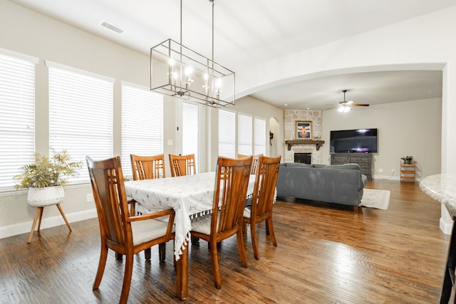 817 Calm Crest Dr, Rockwall, TX 75087 - dining room featuring ceiling fan, dark wood-style floors, a stone fireplace, a chandelier, and arched walkways
