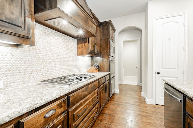 817 Calm Crest Dr, Rockwall, TX 75087 - kitchen featuring appliances with stainless steel finishes, custom exhaust hood, arched walkways, tasteful backsplash, and light wood finished floors