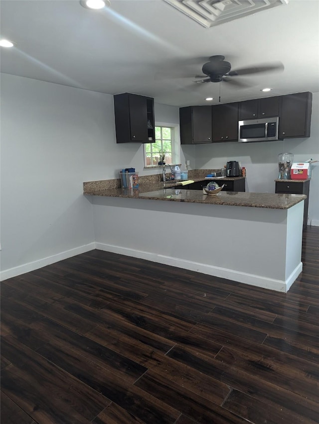 3108 Bideker Ave, Fort Worth, TX 76105 - kitchen featuring stainless steel microwave, dark cabinets, dark wood-style floors, a peninsula, and baseboards
